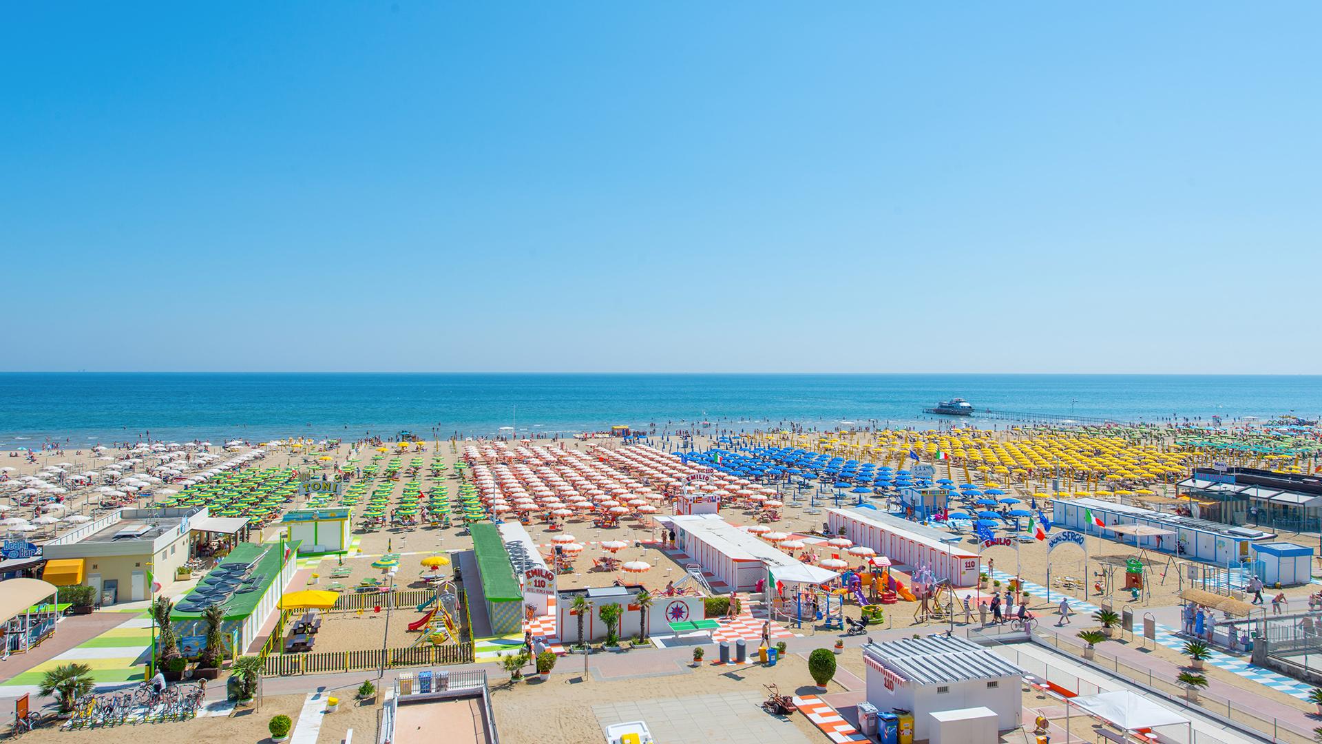 Spiaggia affollata con ombrelloni colorati, mare calmo e cielo azzurro.