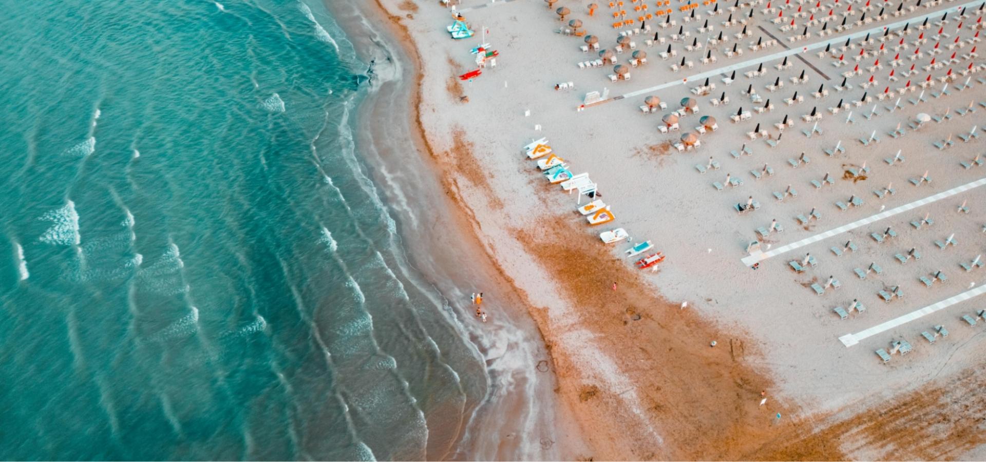 Spiaggia con ombrelloni e sdraio, vista dall'alto, mare calmo e sabbia chiara.