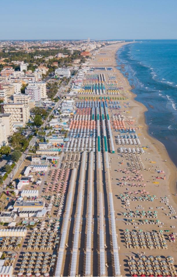 Spiaggia affollata con ombrelloni colorati e mare calmo, vicino a edifici residenziali.